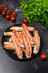 Crab sticks on black plate with parsley and tomatoes at black background
