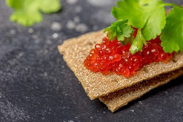 Crispbreads with caviar and parsley at black background