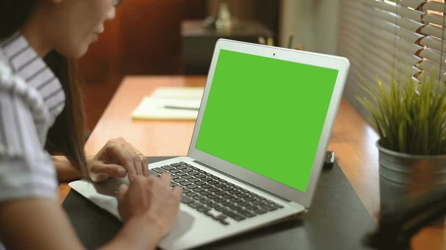 Asian woman works on a Laptop with Mock-up Green Screen 