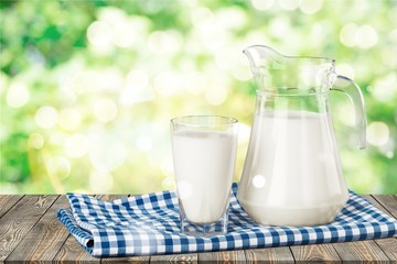 A glass of milk and a milk jug on plaid tablecloth