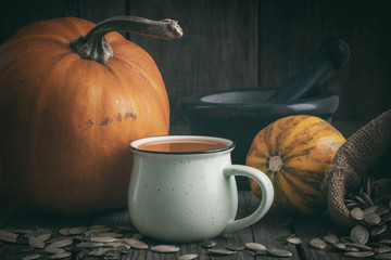 Cup of pumpkin juice, pumpkins, canvas sack of pumpkins seeds  and mortar on wooden table.