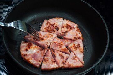 slices of fried ham in a frying pan, laid out in the form of a heart with a fork, breakfast for lovers