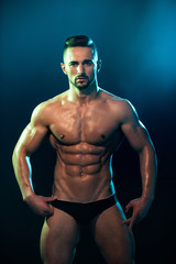 Fototapeta na wymiar Muscular tanned man in a beautiful pose on a white background. Poledancer on background before night show. Seductive young man and advertising of fitness trainings. Club and entertainment for adults.