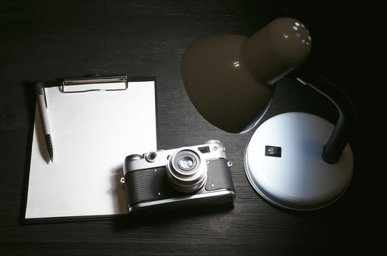 Shot list mockup. Photo ideas list. Photo session contract template. Vintage film photo camera and blank paper page on black wooden table background.