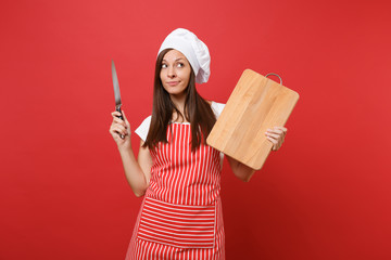 Housewife female chef cook or baker in striped apron, white t-shirt, toque chefs hat isolated on red wall background. Housekeeper woman holding wooden cutting board, knife. Mock up copy space concept.