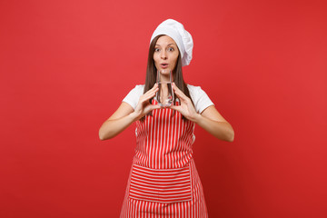 Housewife female chef cook or baker in striped apron white t-shirt toque chefs hat isolated on red wall background. Woman holding drinking clear fresh pure water from glass. Mock up copy space concept