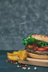 Homemade juicy hamburger with fresh vegetables and potato wedges with spices. On the desk. horizontal view. copy space.