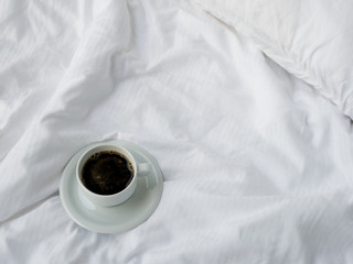 Cup of coffee on white bed, top view