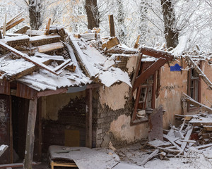 Fototapeta premium The winter. Ruined wooden house on the background of snowy trees and new buildings.