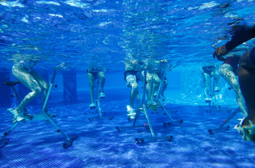 Fitness class doing aqua aerobics on exercise bikes in swimming pool resort hotel