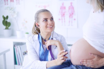 Obraz premium Smiling woman doctor shows pictures on the tablet to pregnant young woman at hospital.