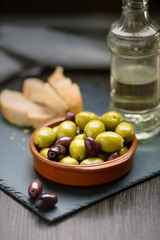 Green and dark olives on a brown greek plate. Olive oil.