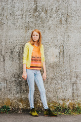 Outdoor portrait of pretty little girl with red hair, wearing orange t-shirt and yellow jacket