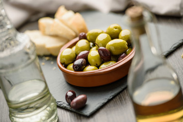 Green and dark olives on a brown greek plate. Olive oil.