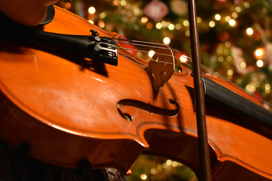 a young person playing the violin with a Chrismas tree in the background
