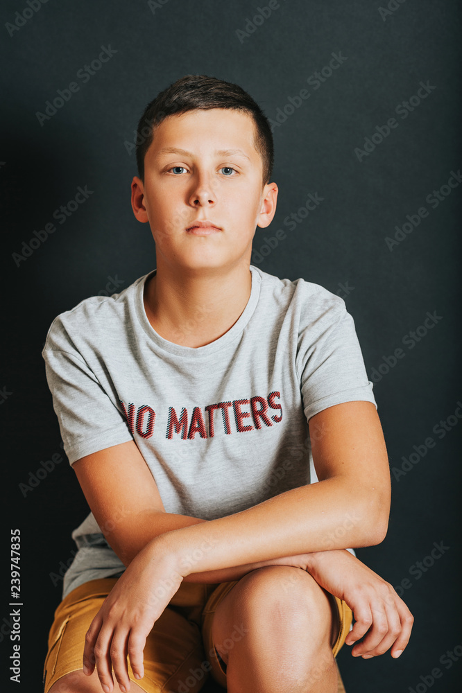 Wall mural studio shot of young teenage boy posing on a black background, wearing t-shirt with sign 