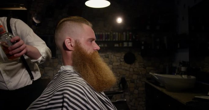 Barber applying sparkling oil to male client in Barbershop slow motion