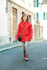 Outdoor fashion portrait of young girl walking down the street, wearing bright red stylish coat