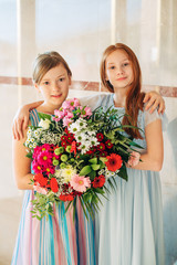 Fototapeta na wymiar Two beautiful girls wearing occasion dresses, holding big flower bouquet