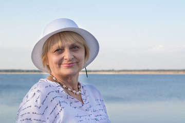 Smiling elderly lady rests in nature near sea