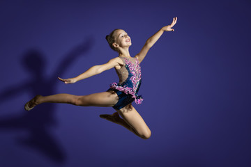 Fototapeta na wymiar girl gymnast performs the jump. Frozen motion. Violet background. A child in a bathing suit for rhythmic gymnastics