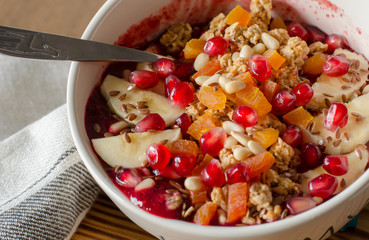 Smoothie acai bowl topped with pomegranate, bananas, flaxseeds, cedar seeds, dried apricot and granola. Acai breakfast superfoods smoothie bowl and spoon. close up, angle view