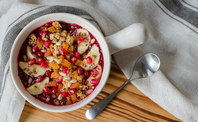 Smoothie acai bowl topped with pomegranate, bananas, flaxseeds, cedar seeds, dried apricot and granola. Acai breakfast superfoods smoothie bowl and spoon. Overhead, top view.