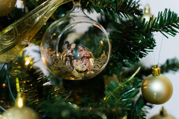 Nativity scene in In golden christmas tree with balls and bokeh blurred leds