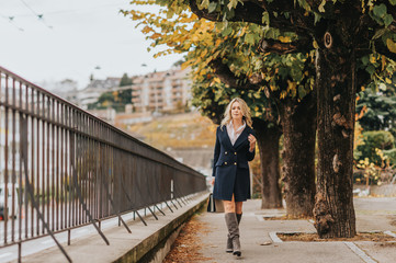 Outdoor portrait of beautiful woman wearing dark blue jacket dress, model walking down the street, holding a bag