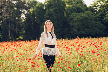 Outdoor portrait of beautiful woman with blond hair, wearing white blouse, posing in poppy field