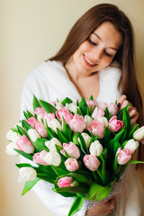 A young woman looks at her big bouquet of tulips. Sunny spring morning.