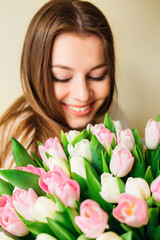 Young beautiful woman closing her eyes and smiling behind the big pink tulips flowers bouquet.