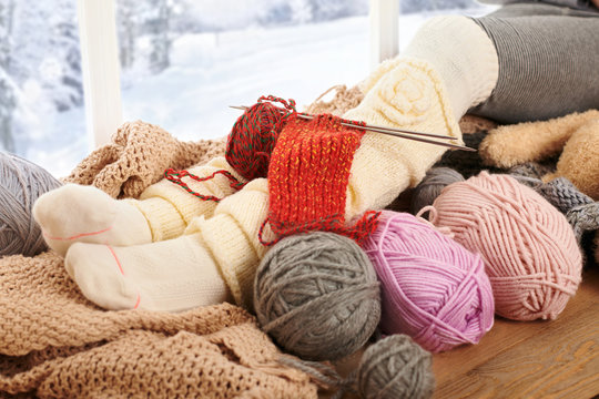 Child legs in warm socks are on a window sill with wool yarns.