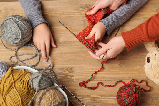 Child girl is learning to knit. Colorful wool yarns are on the wooden table. Hand closeup.