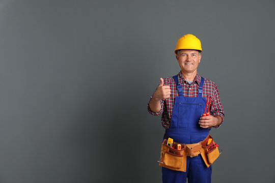 Electrician with tools wearing uniform on gray background. Space for text