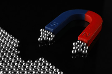 Magnet attracting chrome balls on black background. Business leadership concept