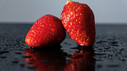 Rojas frutillas frescas con gotas de agua sobre ellas, luz directa y superficie negra