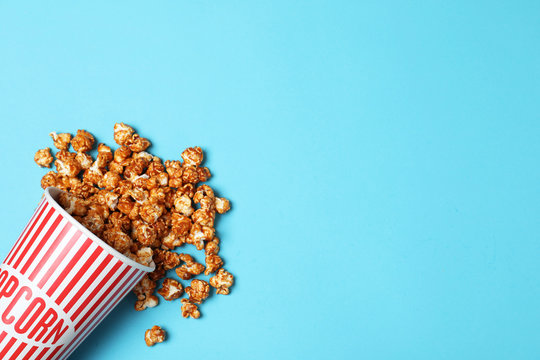 Overturned paper cup with caramel popcorn on color background, top view. Space for text