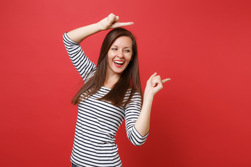 Portrait of laughing young woman in striped clothes looking and pointing index fingers aside isolated on bright red wall background. People sincere emotions, lifestyle concept. Mock up copy space.