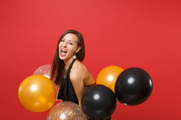 Fototapeta na wymiar Beautiful happy young woman in black dress celebrating holding air balloons isolated on red background. St. Valentine's, International Women's Day Happy New Year birthday mockup holiday party concept.