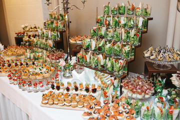 Beautifully decorated catering banquet table with profiteroles, salads and cold snacks. Variety of tasty delicious snacks on the table. Wedding table serving. Meat and vegetables