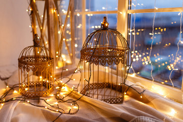 Cages for birds covered with garland with yellow lights. Cozy winter or autumn morning at home. Warm blanket, garland with lights Swedish concept hygge.