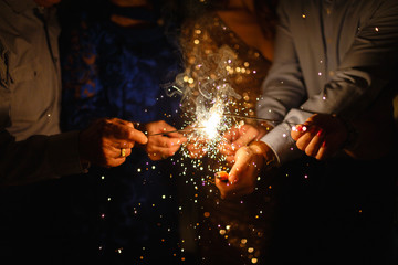 Fototapeta na wymiar New year party burning sparkler closeup in hands on black background. company of people holding glowing holiday sparkling hand fireworks, shining fire flame. Christmas light.