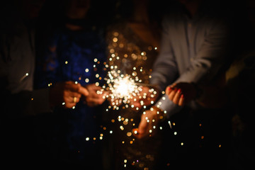 New year party burning sparkler closeup in hands on black background. company of people holding glowing holiday sparkling hand fireworks, shining fire flame. Christmas light.