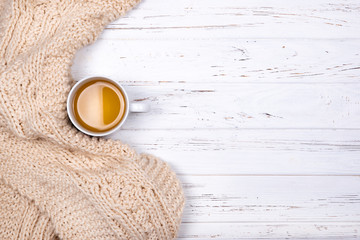Single cup of tea and beige plaid on white wooden background.