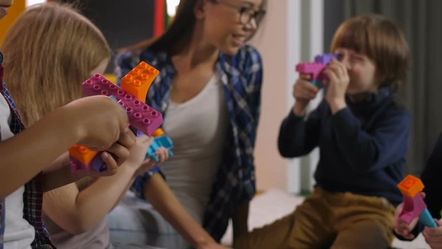 Carefree preschool multi ethnic children and teacher playing with colorful plastic toy blocks in kindergarten. Diverse kids building with construction blocks and having fun with developing toys.