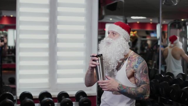 Fitness instructor Santa Claus in the gym drinks water from a shaker and gets angry.