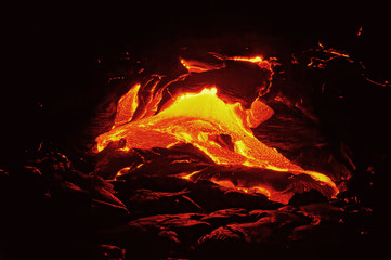 Scenic view of a part of a lava flow in the dark, the hot lava shows up in yellow and red shades -...