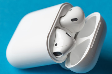 White wireless bluetooth earphones or headphones and white box for storage and charging on blue...