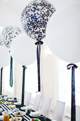 Festive dinner table decor. White and black balloons hang over the restaurant table served with delicious food